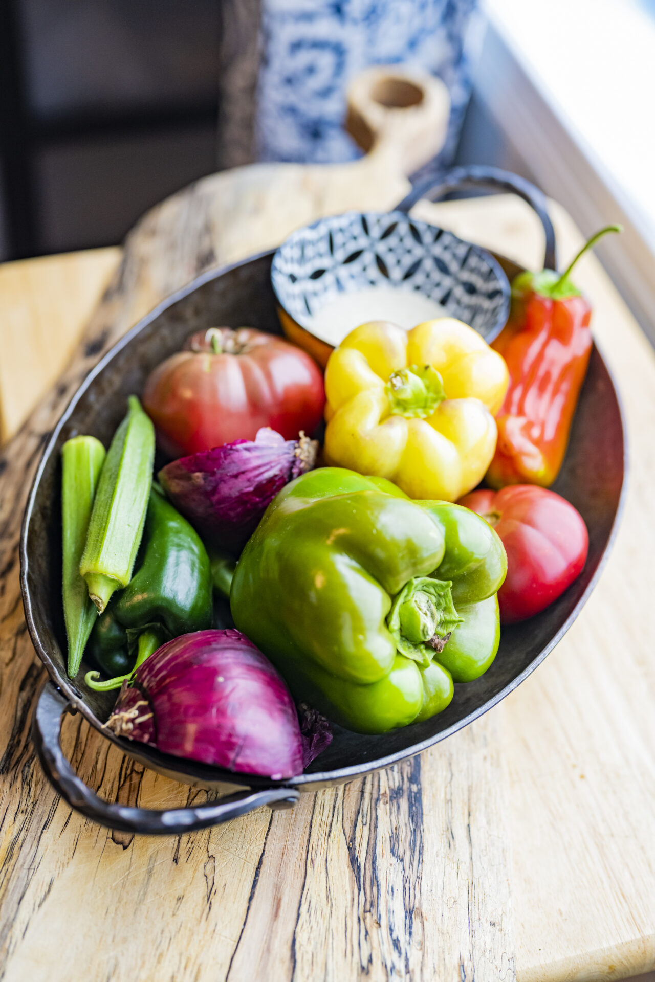 Dish storing fresh vegetables, like bell peppers, okra, red onion, and tomato.