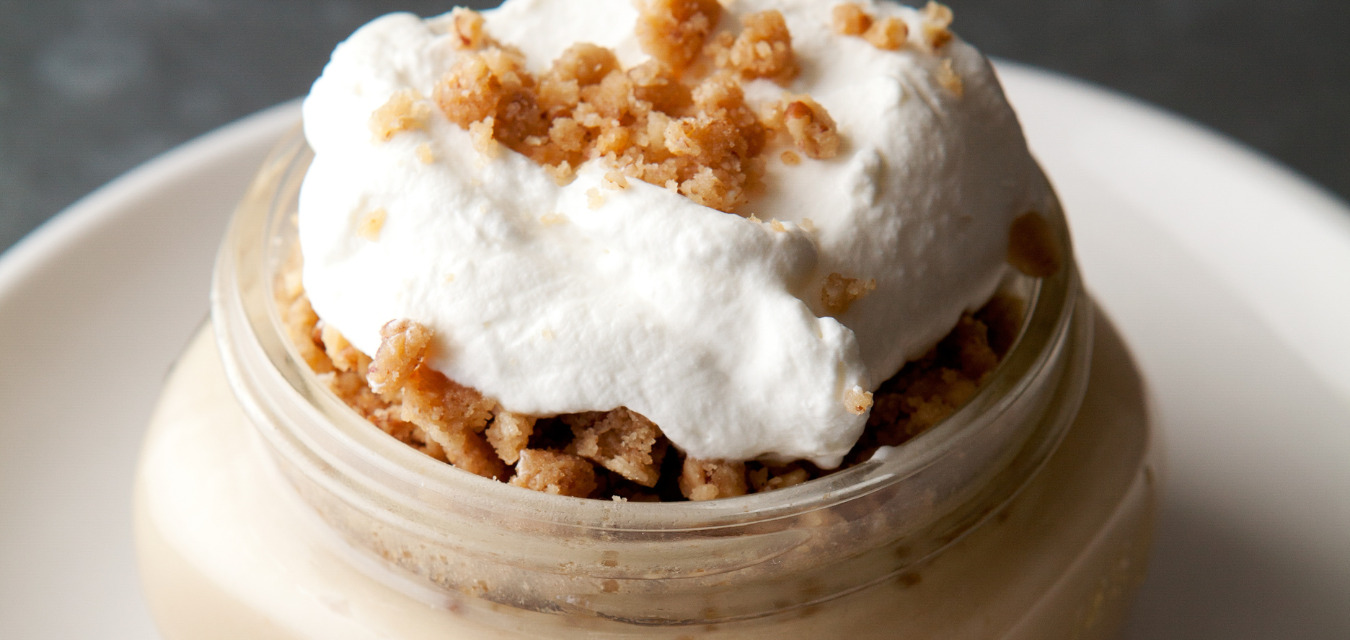 Maple-Whiskey Pudding in a short mason jar topped with whipped cream and bacon crumble