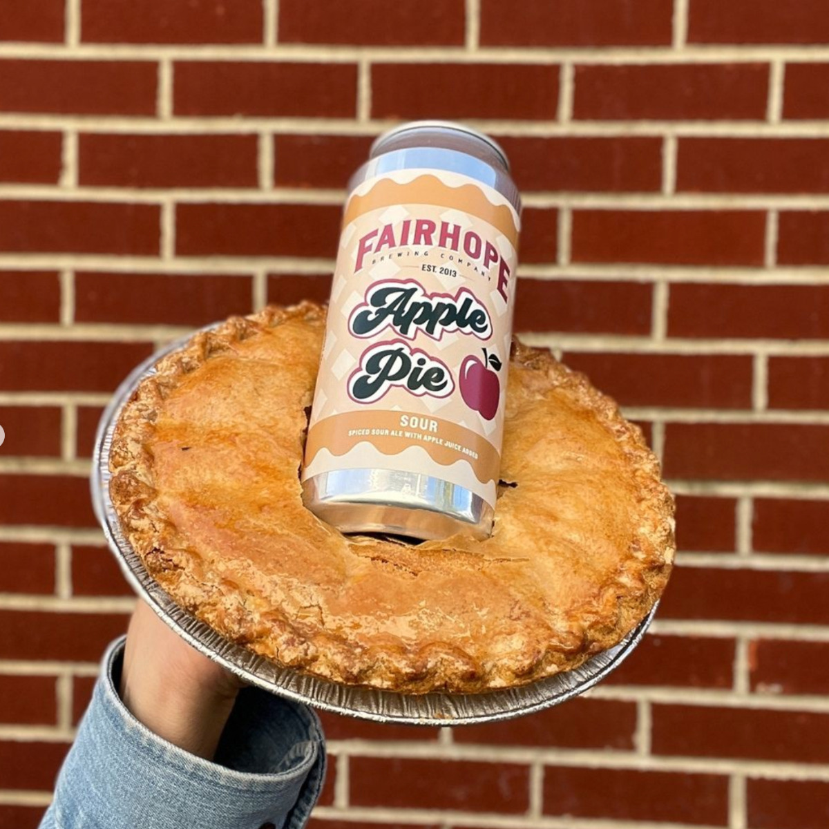 Fairhope Brewing Co. Sour Apple Pie Ale in a 16 oz can, stuck into an apple pie