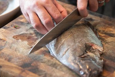 Image of how to fry a fish as a man is scoring the skin and flesh of the fish
