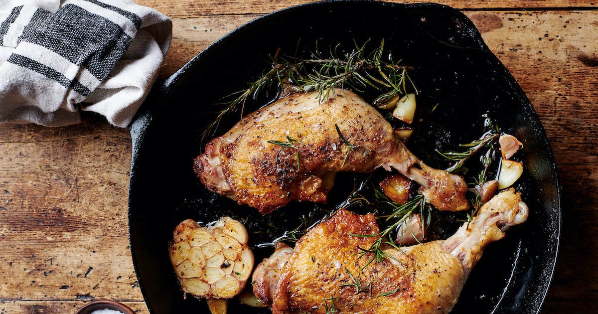 Two chicken thighs in a skillet with garlic and rosemary