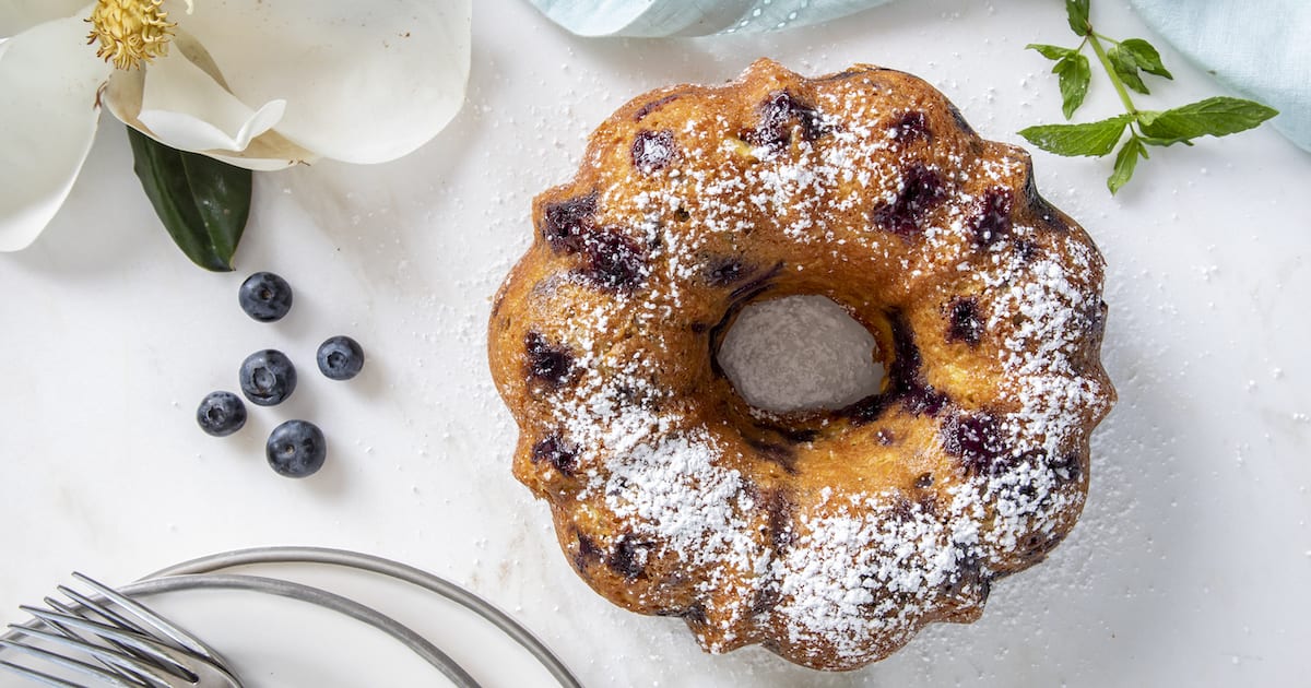 A blueberry bundt cake surrounded by a magnolia flower and mint leaves