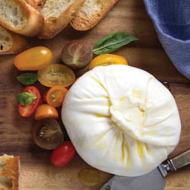 Burrata with sliced tomatoes and other vegetables next to it.