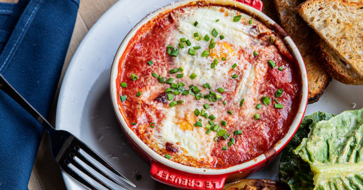 Baked eggs in purgatory in a small Le Crueset dish with salad and toast