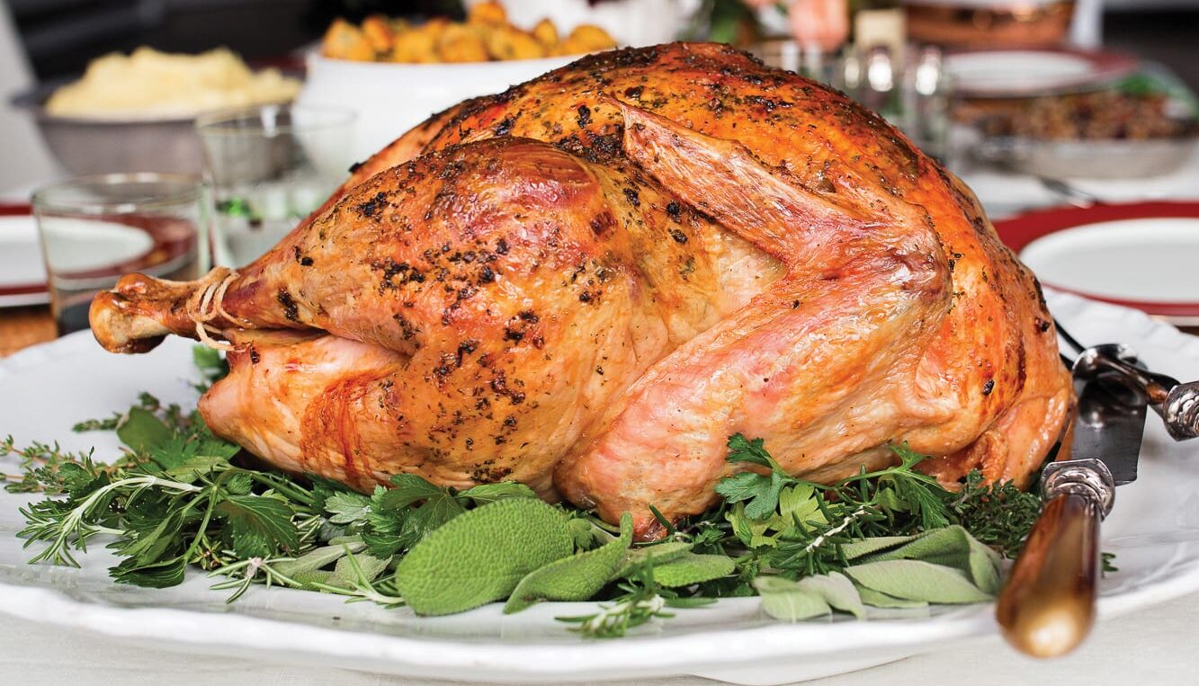 Roasted turkey on platter with herb garnishes surrounded by thanksgiving sides