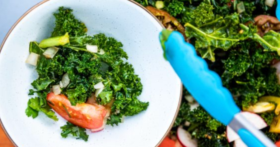 Photograph of the kale salad being served into another bowl with tongs, a camping food