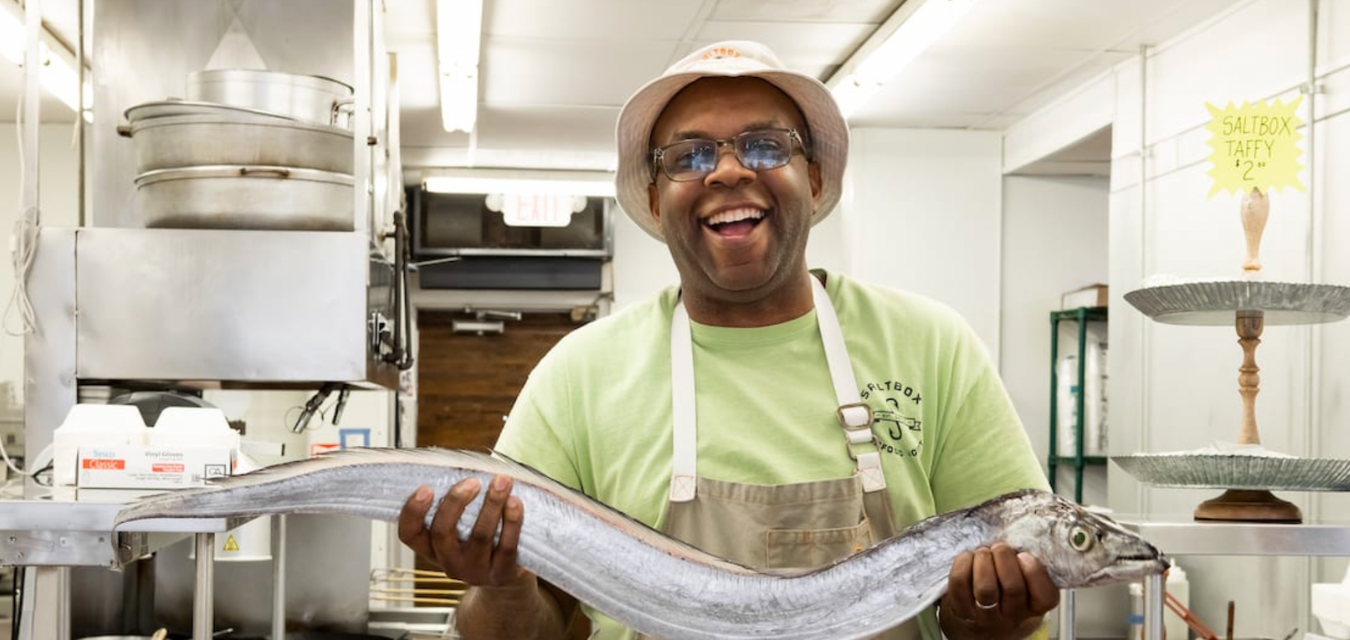 Photograph of the Chef of Saltbox Seafood holding a large fresh fish, making it where to eat in North Carolina
