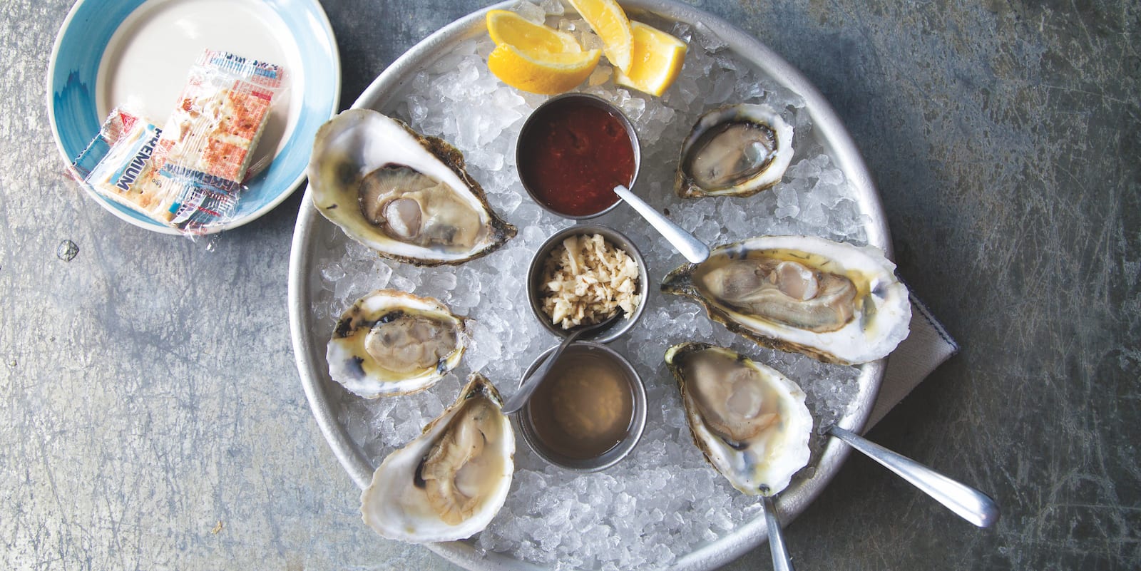 Learn how to shuck oysters at home to create this dreamy half dozen raw oysters on a plate of ice with cocktail sauce, mignonette, and horseradish.