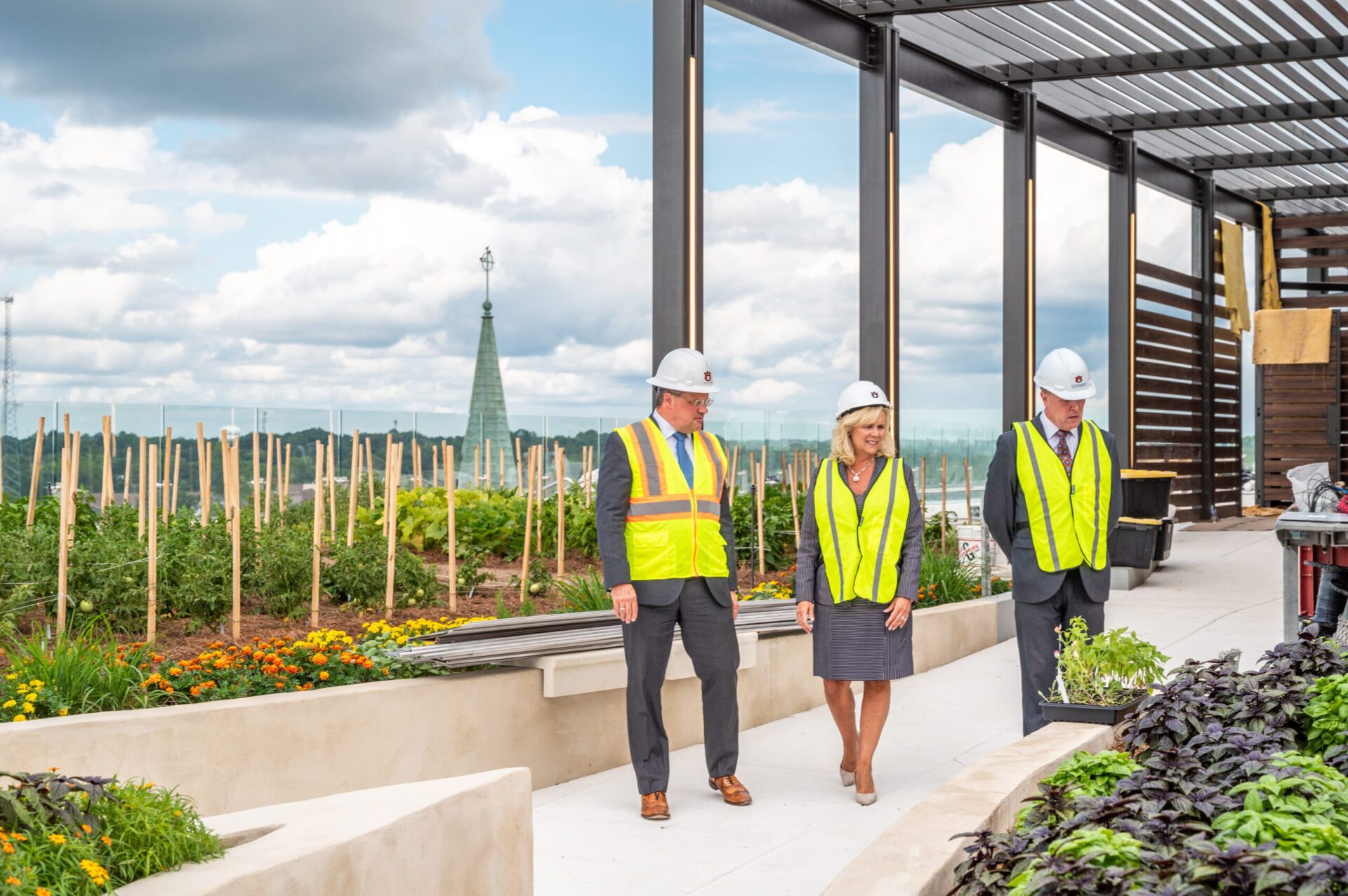Photograph of three people in construction gear walking on the rooftop terrace with garden behind them