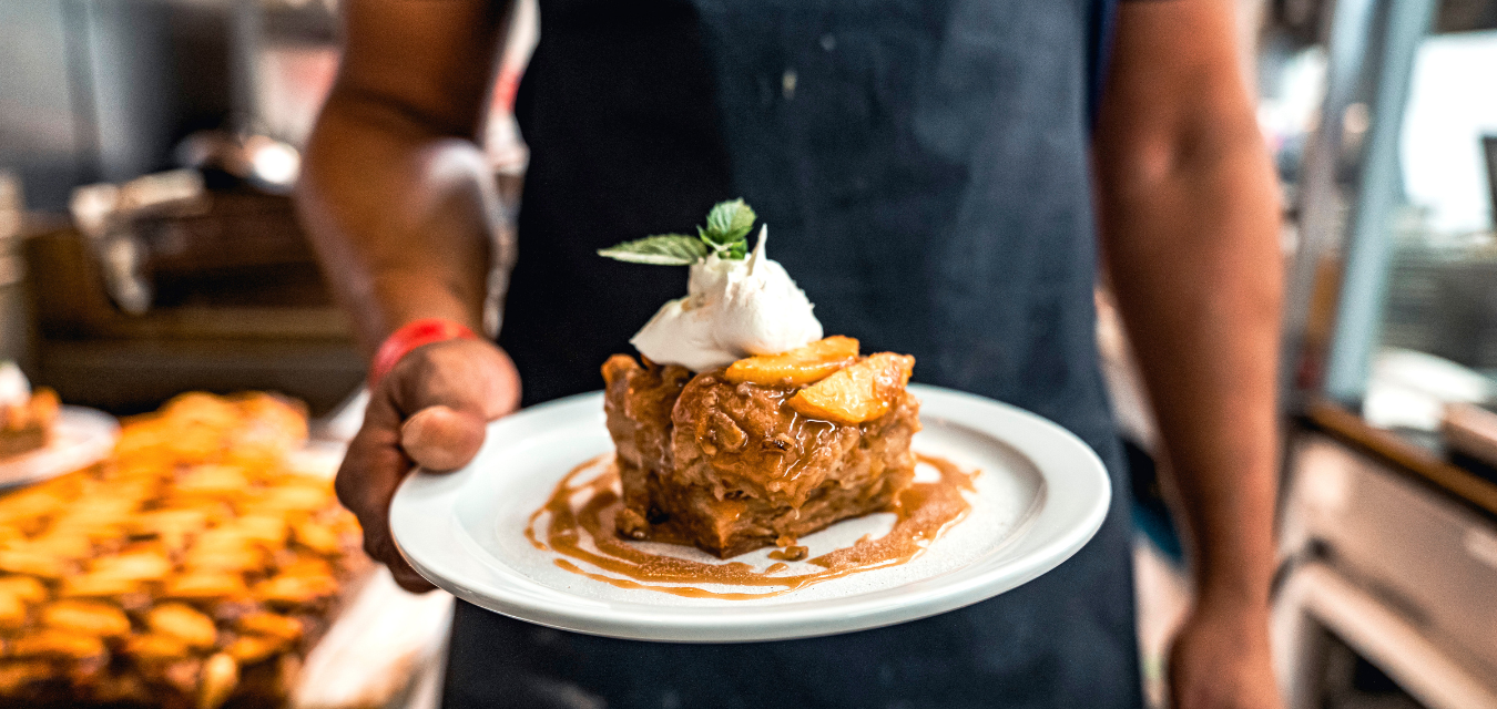 Chris Williams highlighting South Carolina cuisine by holding a bread like dessert covered in a brown glaze and vanilla ice cream. 