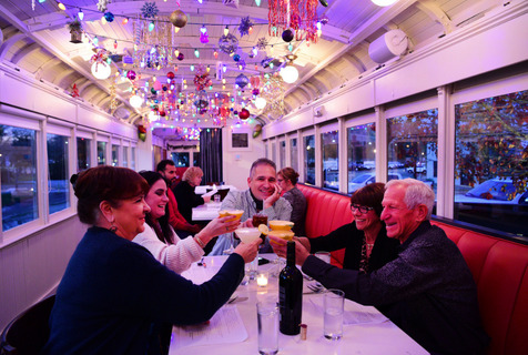 Group of diners toasting their drinks in the holiday-decorated train car at LOLA in Covington, Louisiana