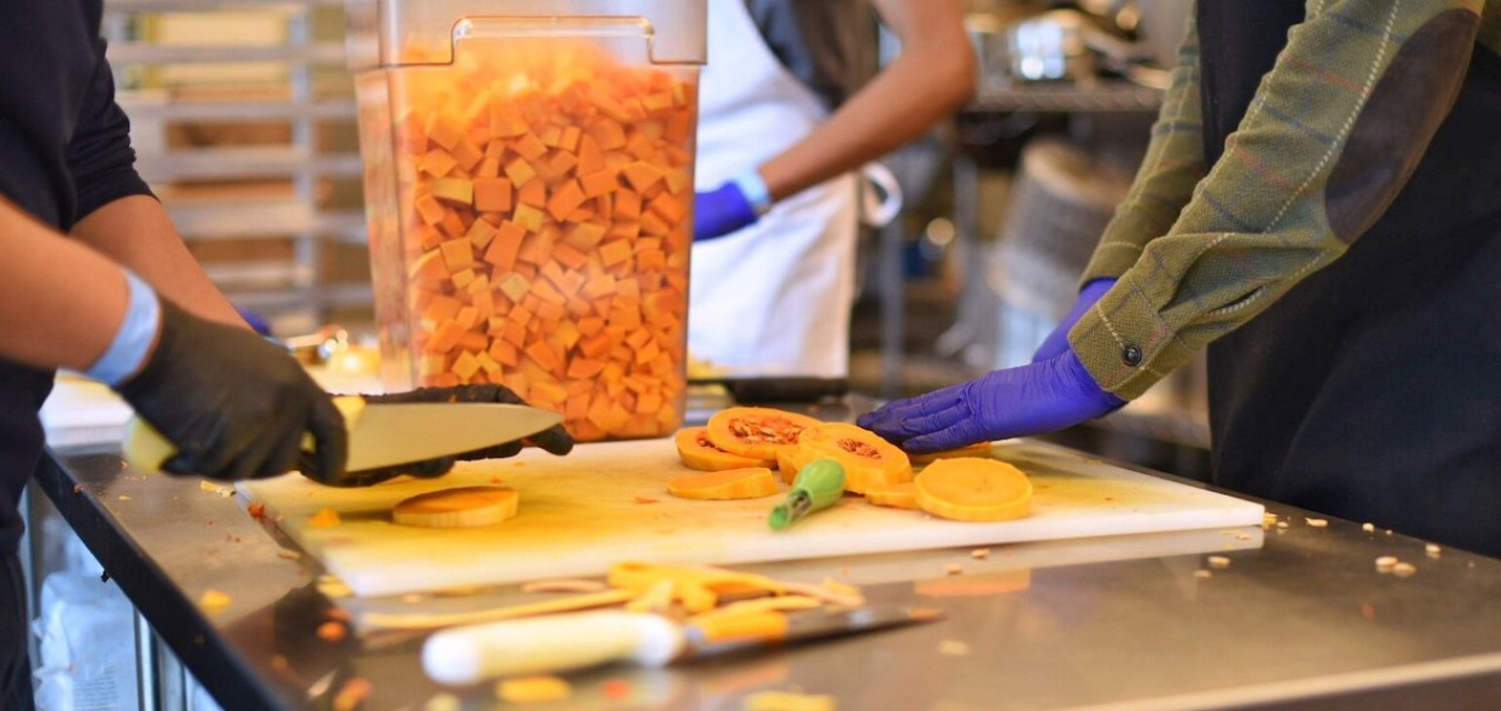 Squash being chopped by two gloved hands on a metal food prep surface