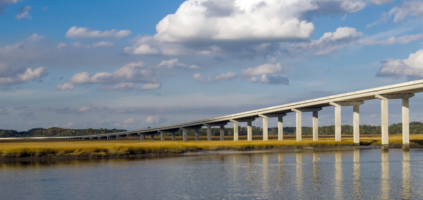 The National Scenic Byway where sprawling areas of preserved land paved with live oaks usher you over the intercoastal waterway and onto Edisto. A big blue sky with white fluffy clouds. 