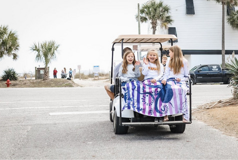  Three young girls riding a gold cart to Edisto Beach. They are smiling and waving at the photographer. 