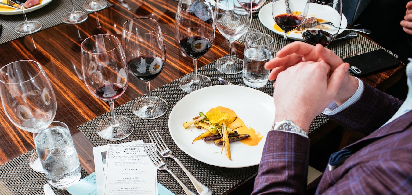 A plate of food and many glasses on wine on a table at a dinner at Charlotte Wine + Food Week