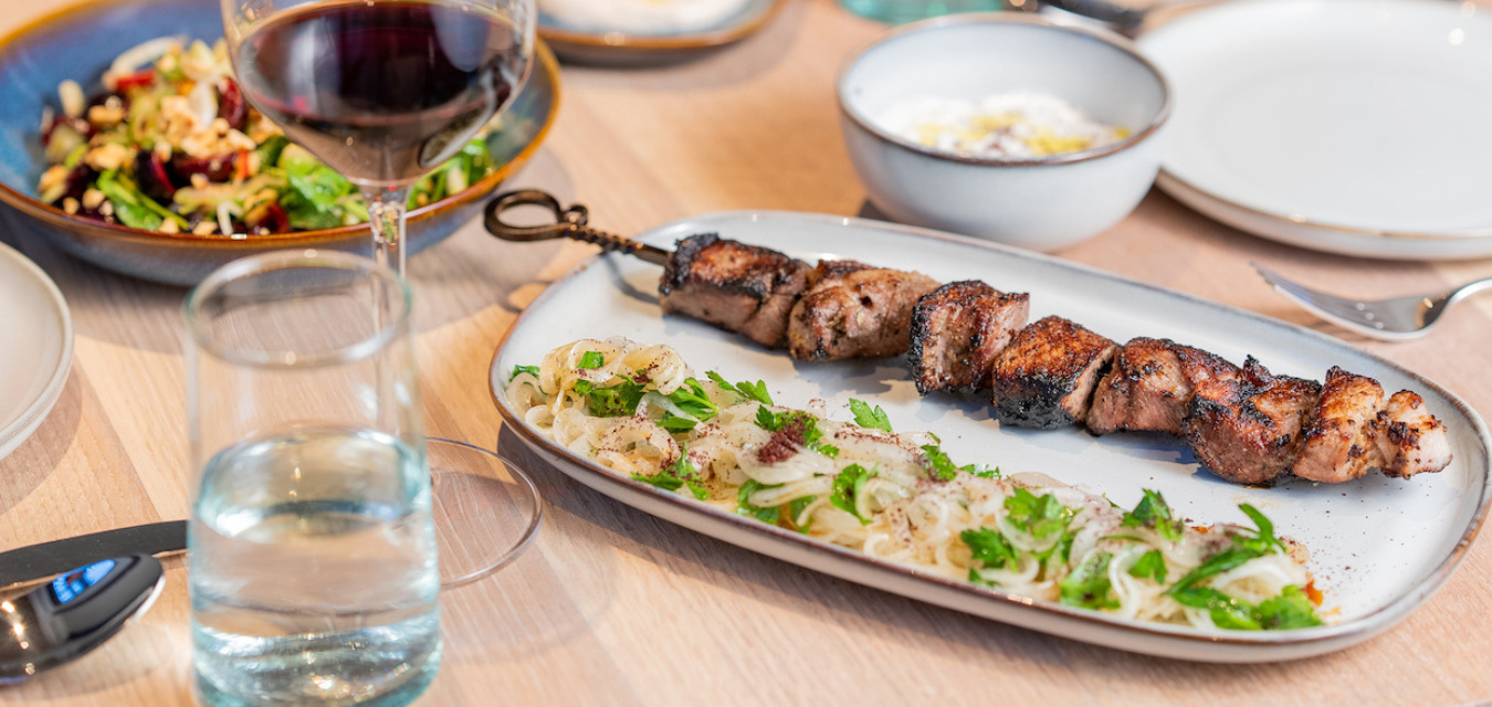 Pork Skewers on a plate with onion salad and bowl of tzatziki