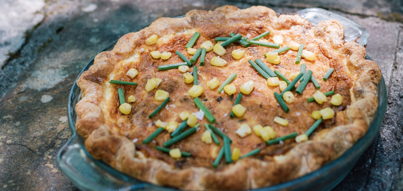 A finished Corn Custard Pie with corn and chives on top resting in the sunlight, one of Cox's savory pie recipes
