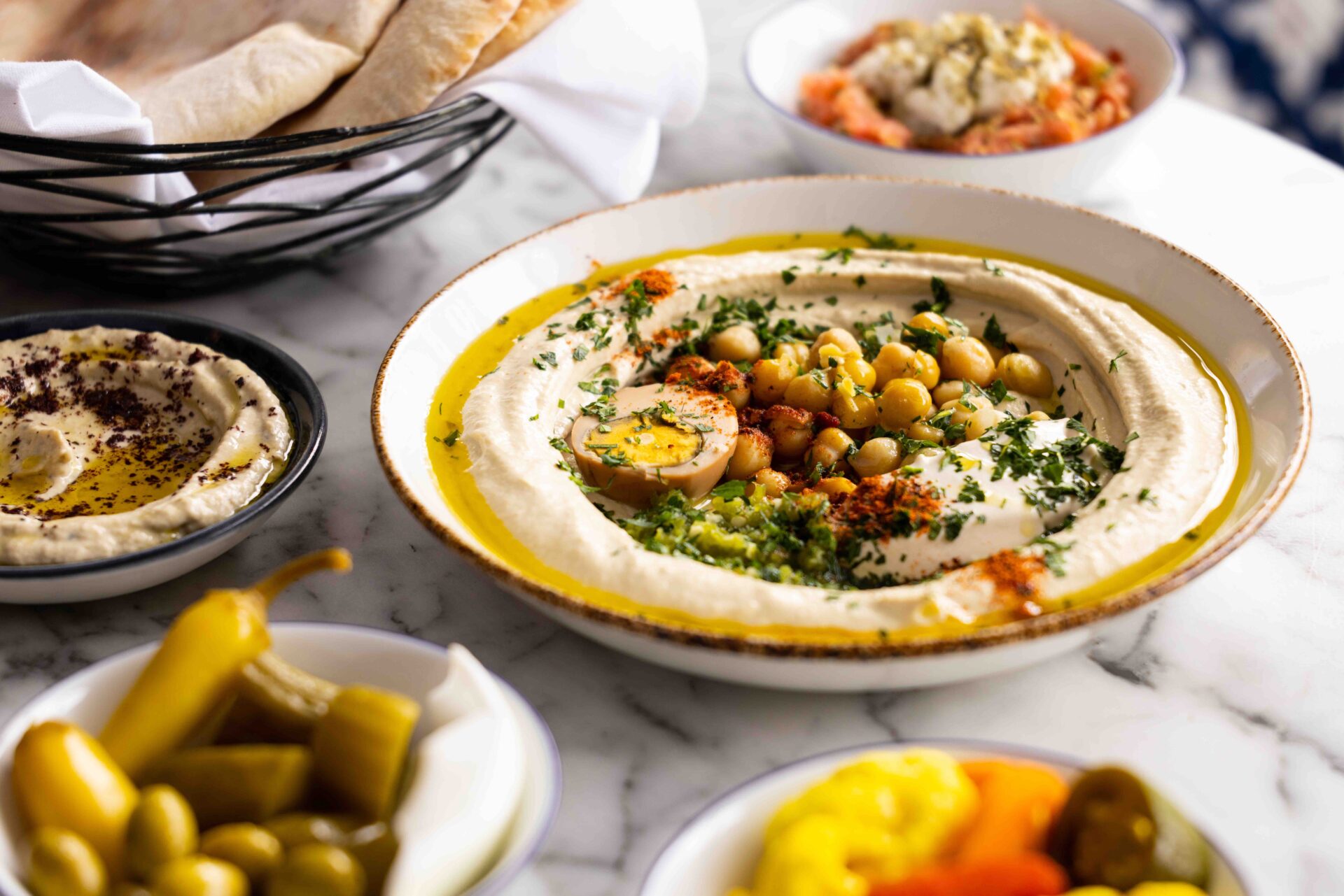 Hamsa Baba Ganoush in a white bowl topped with chickpeas, egg, and herbs