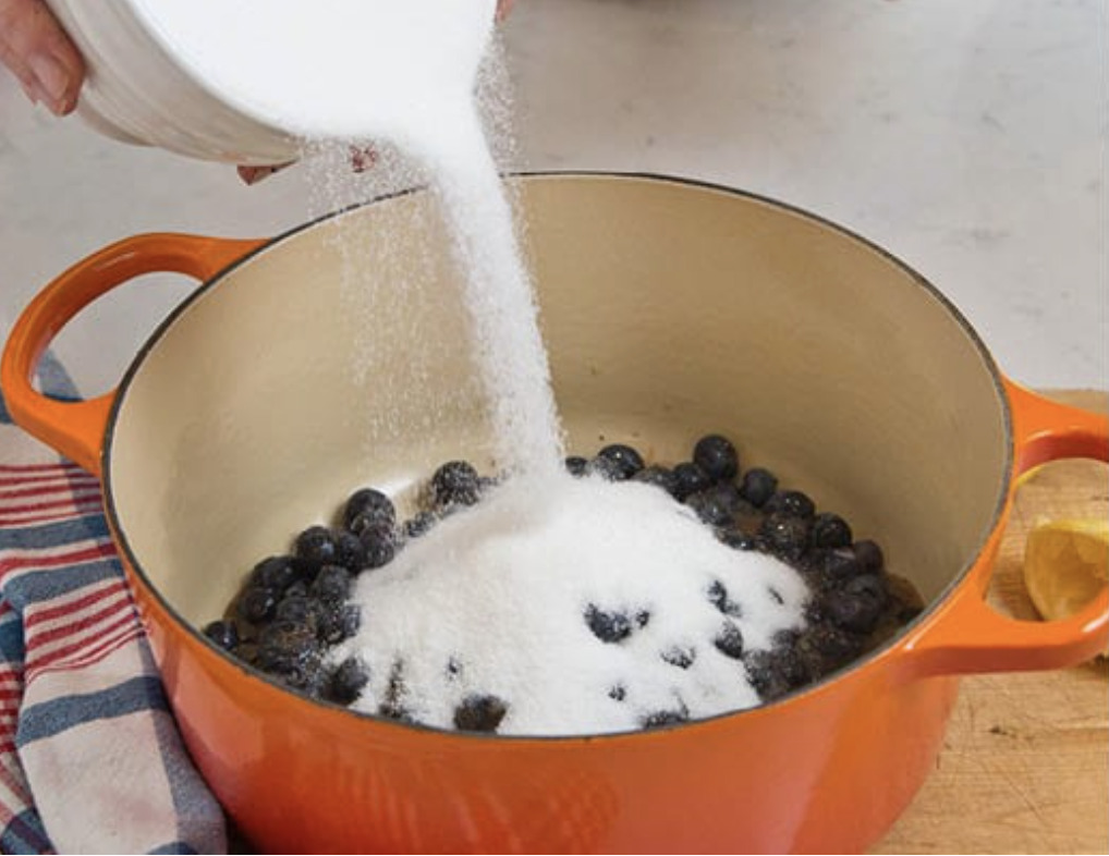 Homemade Jam Step 2: pouring sugar over top of blueberries in an enamelware pot