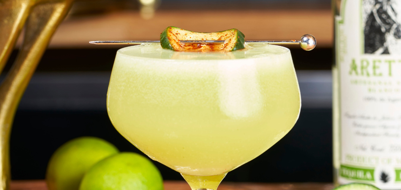Horse Play, a lime green drink with a roasted cucumber and horseradish skewered and placed at the top of the glass.