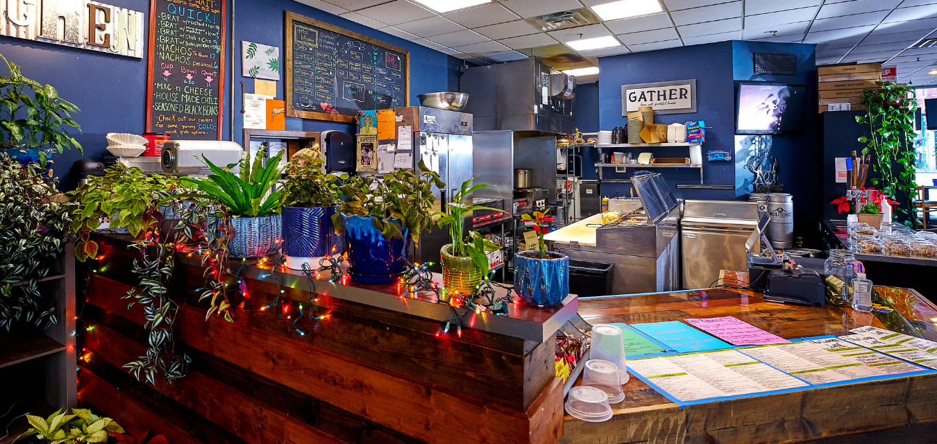 The front counter at The Loopy Leaf, one of seven featured West Virginia restaurants. Lots of plants sit on the counter. Colorful menu and Christmas lights. 