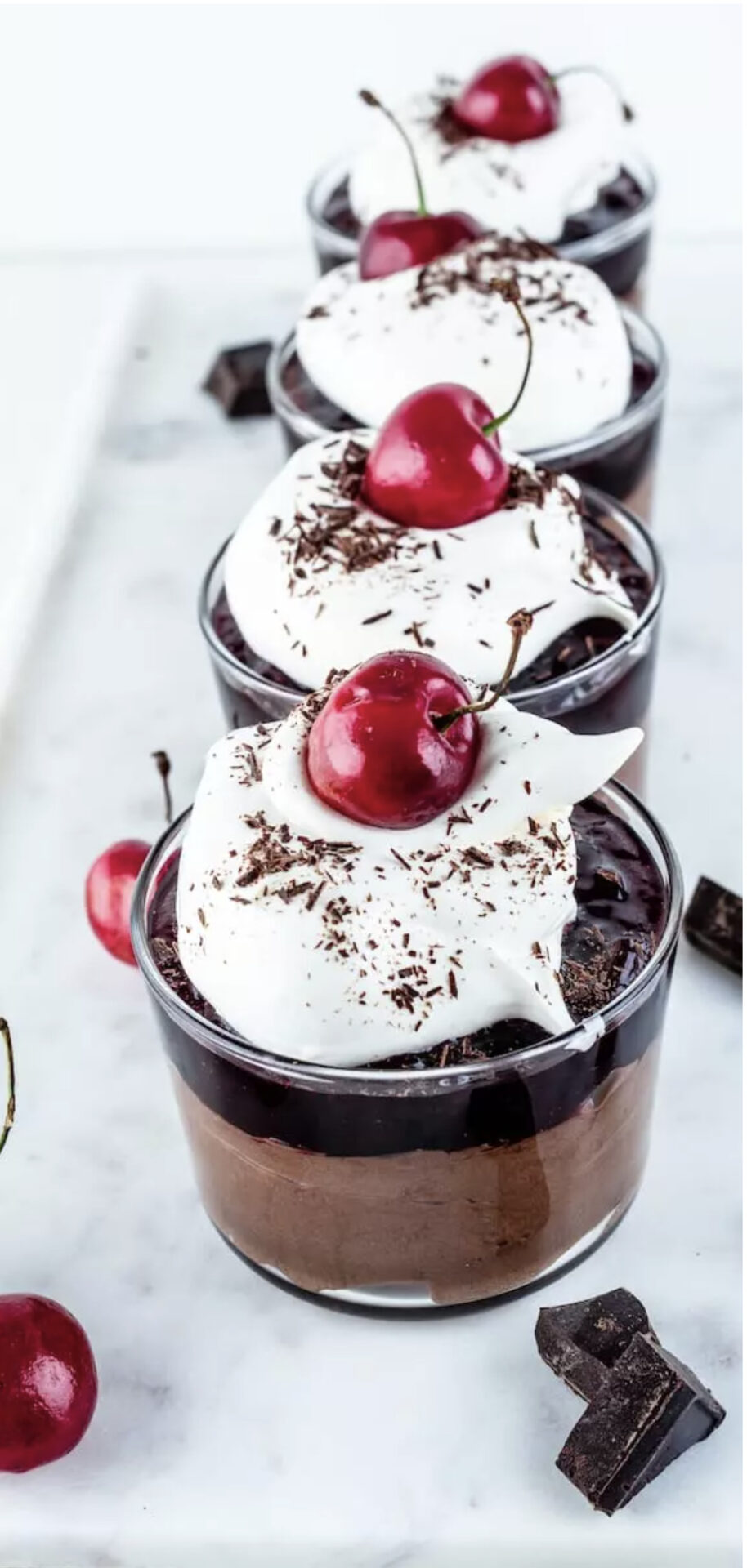 Four chocolate cherry mousse cups with cherries on top are a festive no-bake dessert