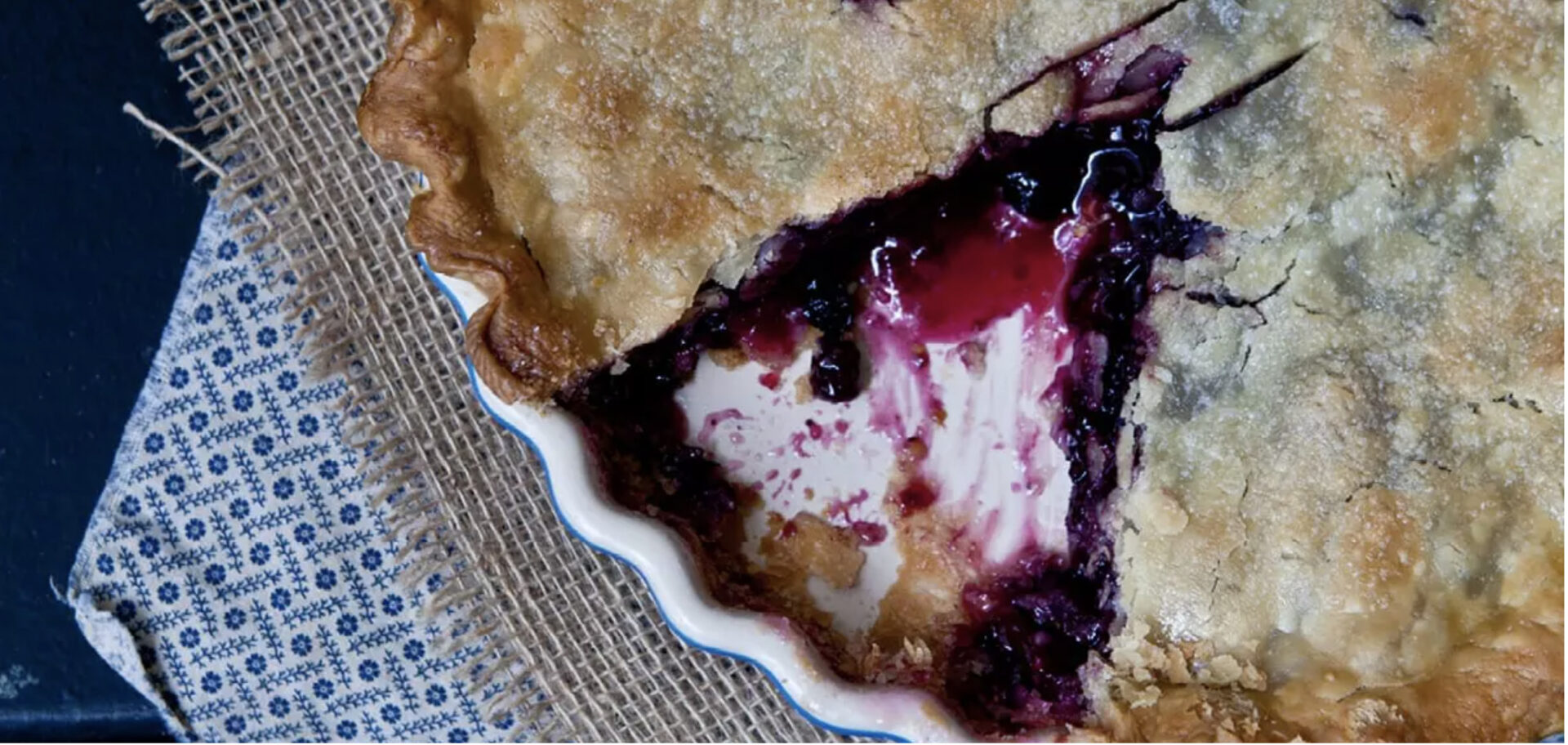 Amethyst blueberry pie nestled in a pie plate with a slice removed
