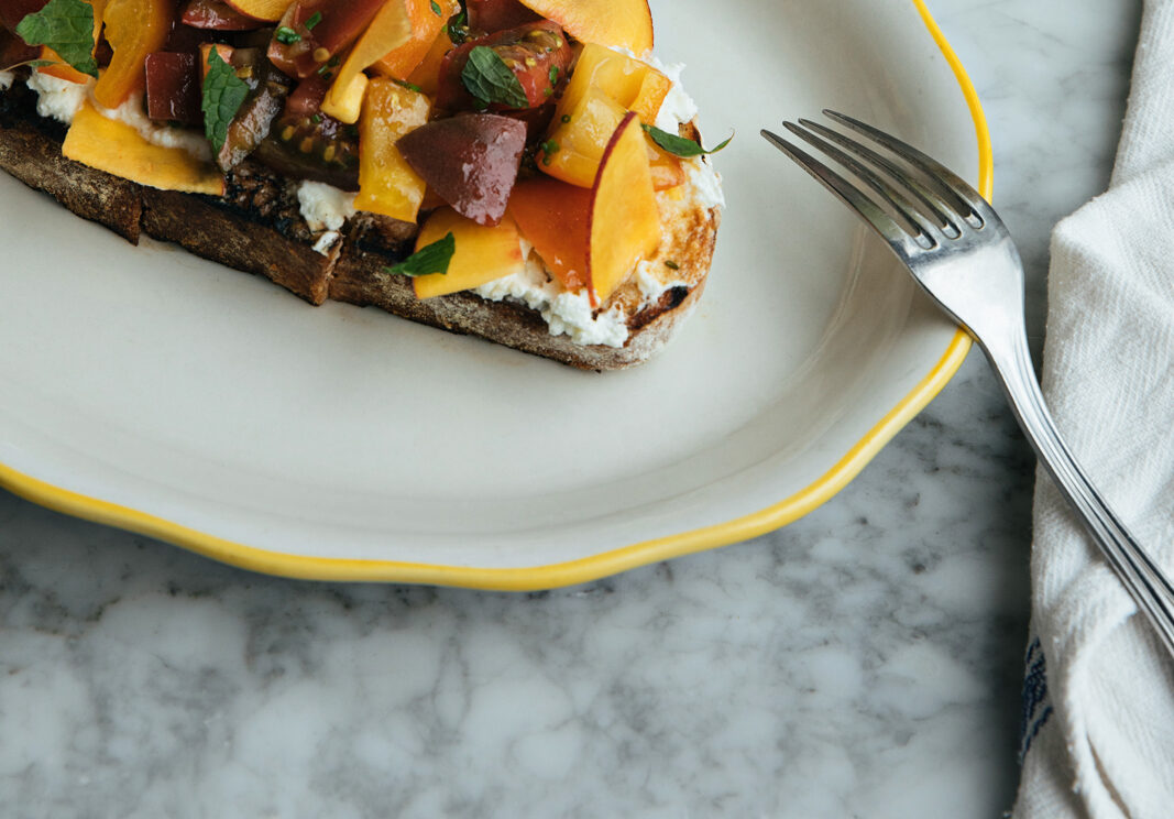 Tomato and peach toast sit on a plate.