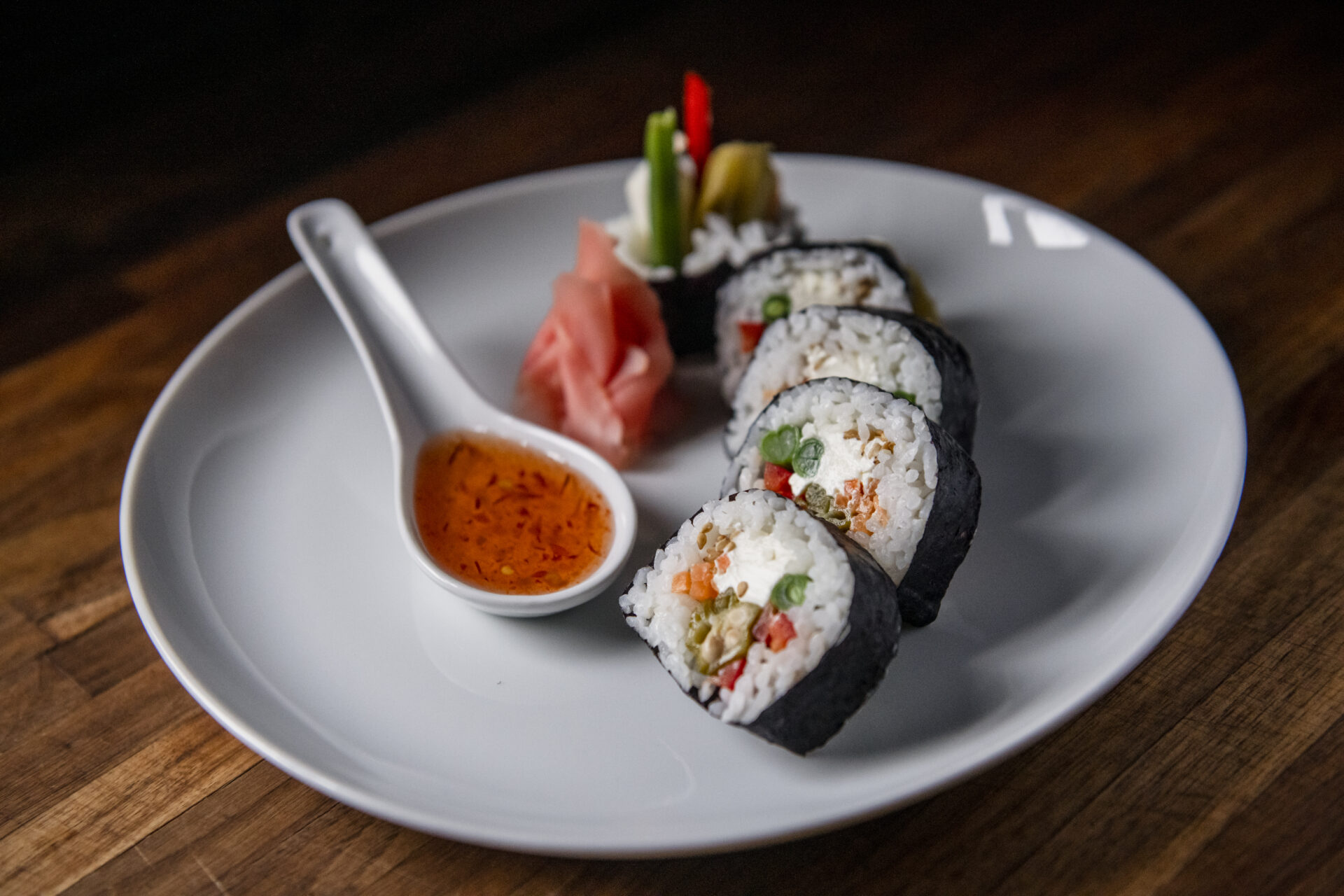Five sushi rolls sit on a white plate with a spoon full of sauce.