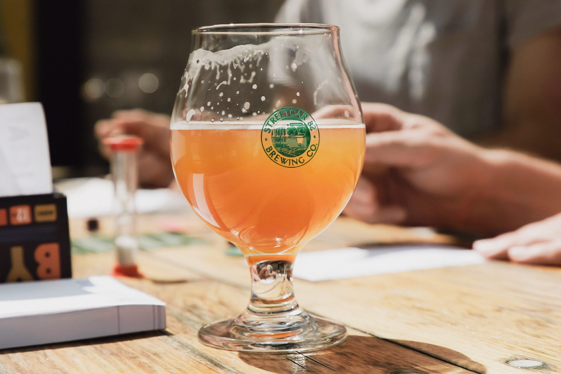 Image of a glass of light beer sitting on a wooden table at brewery with Streetcar 82's logo on the center of the glass.