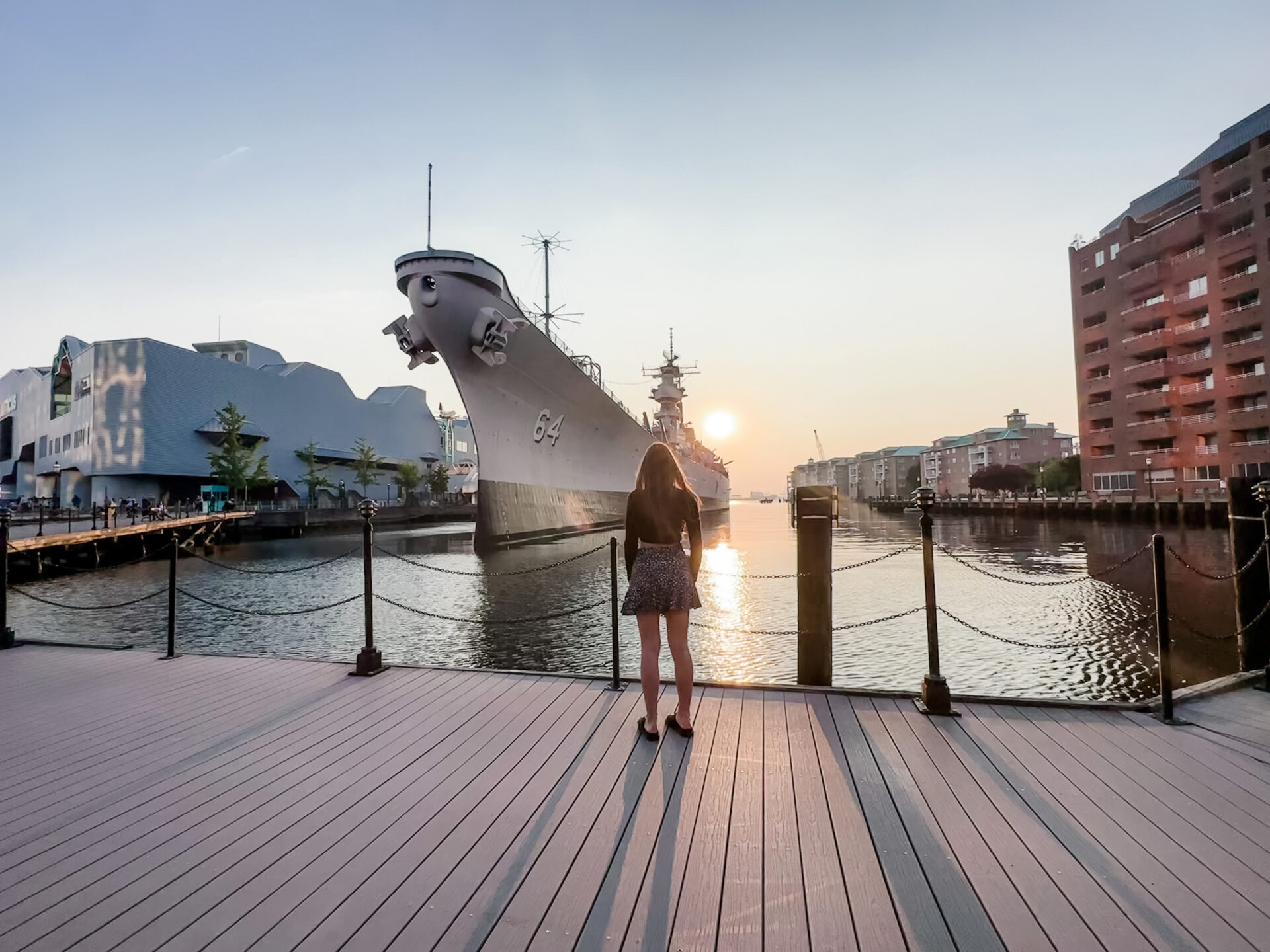 Eastern virginia: a picture of a battleship in the harbor at Norfolk with a girl looking at it while standing on the dock 