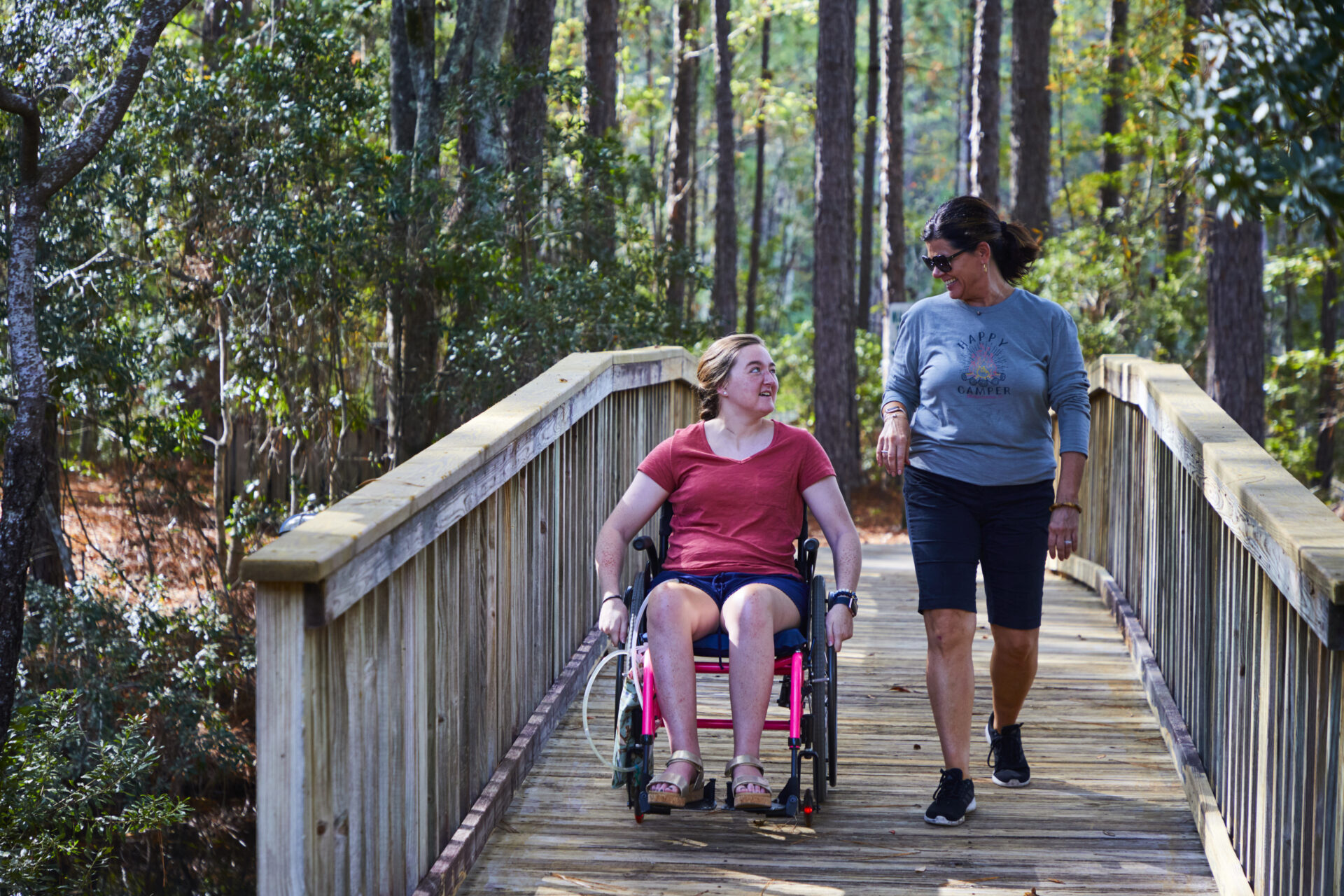 Two women, one walking and one in a wheelchair, enjoying a stroll down an accessible trail in South Carolina Lowcountry.