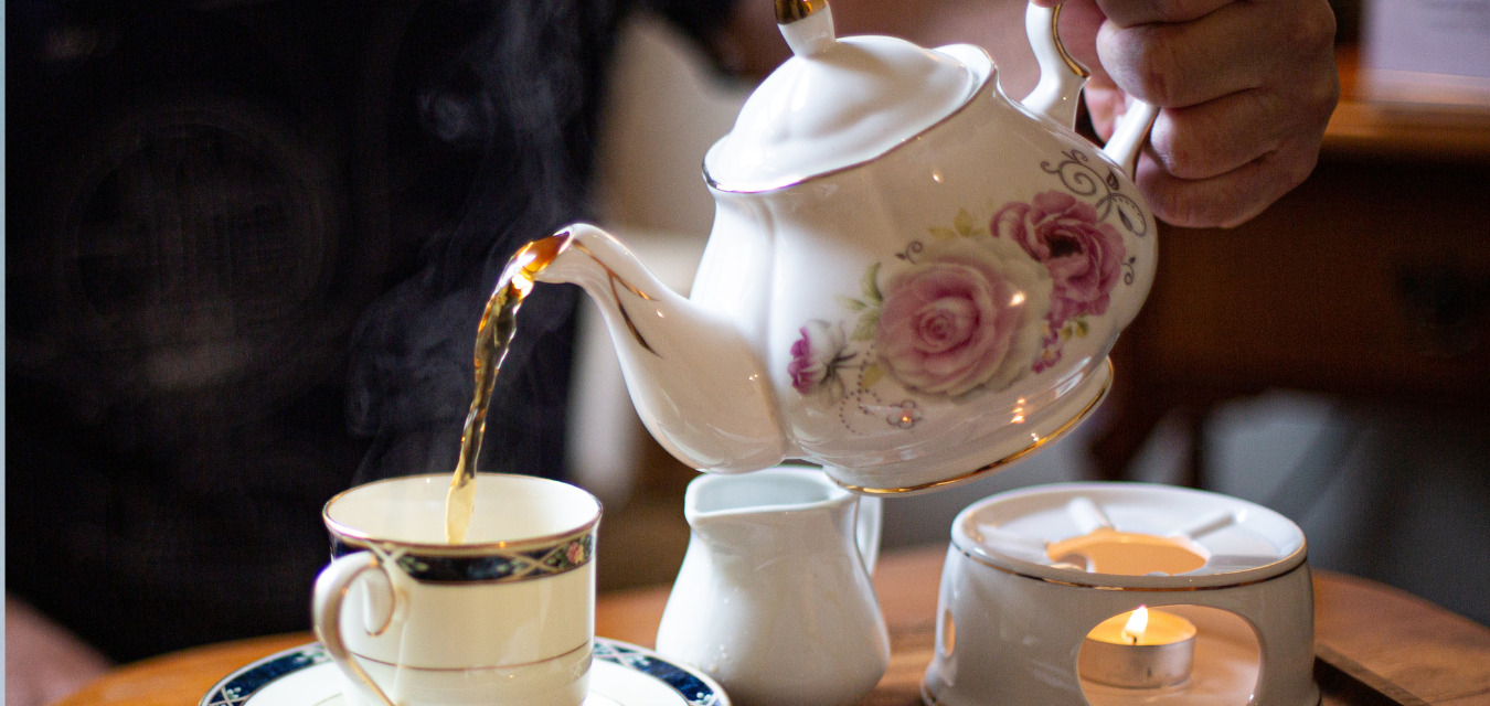 philosopher's tea house: someone holding a white floral tea kettle and pouring tea into a glass from it