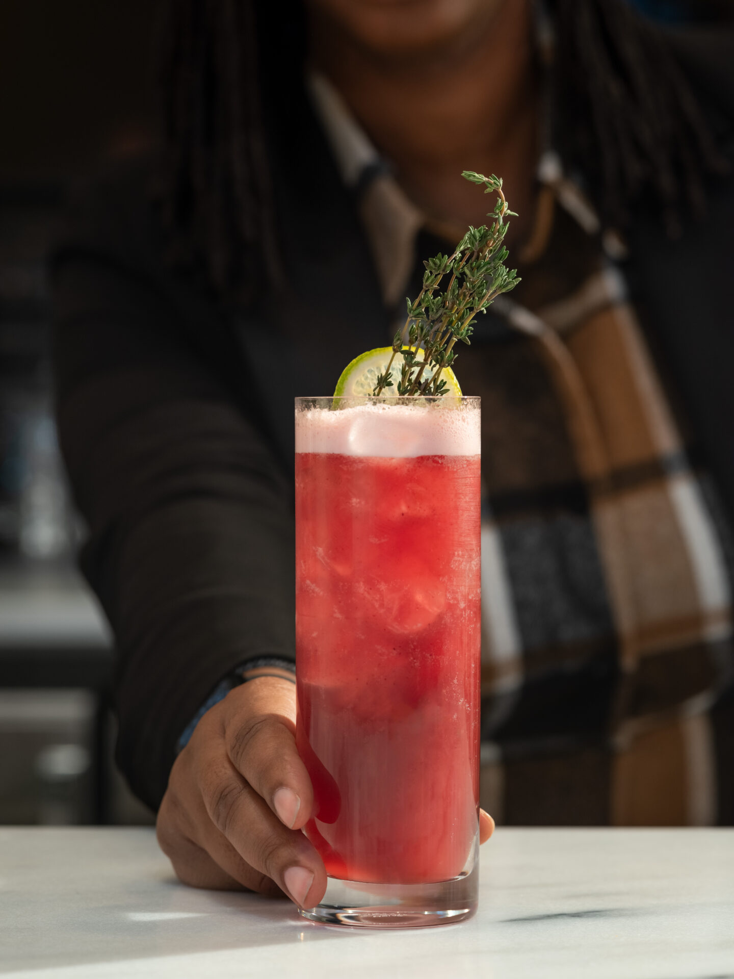 A pink drink topped with thyme is handed across the counter at Dear Charles