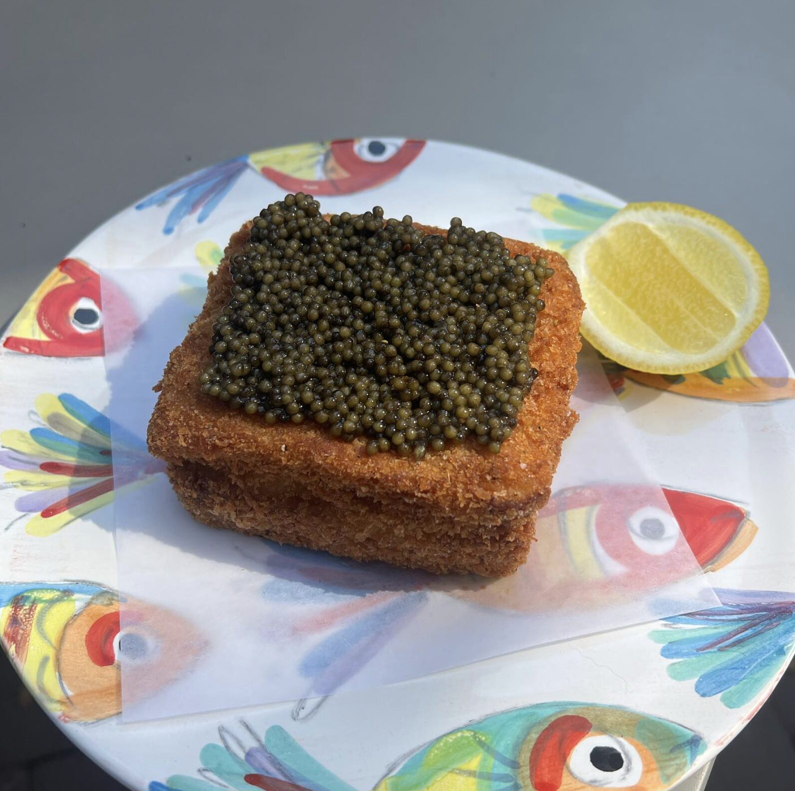 Costa Caviar on brioche served with lemon on a fish patterned plate