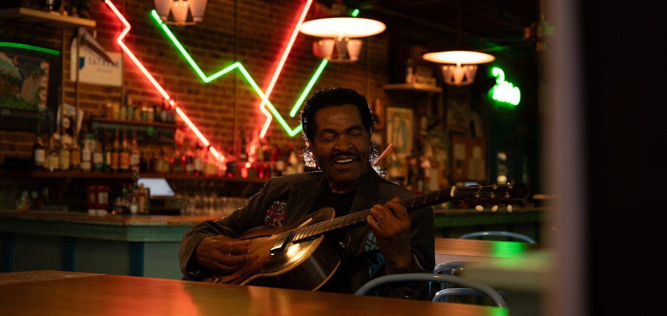 Bobby Rush playing guitar in a bar.