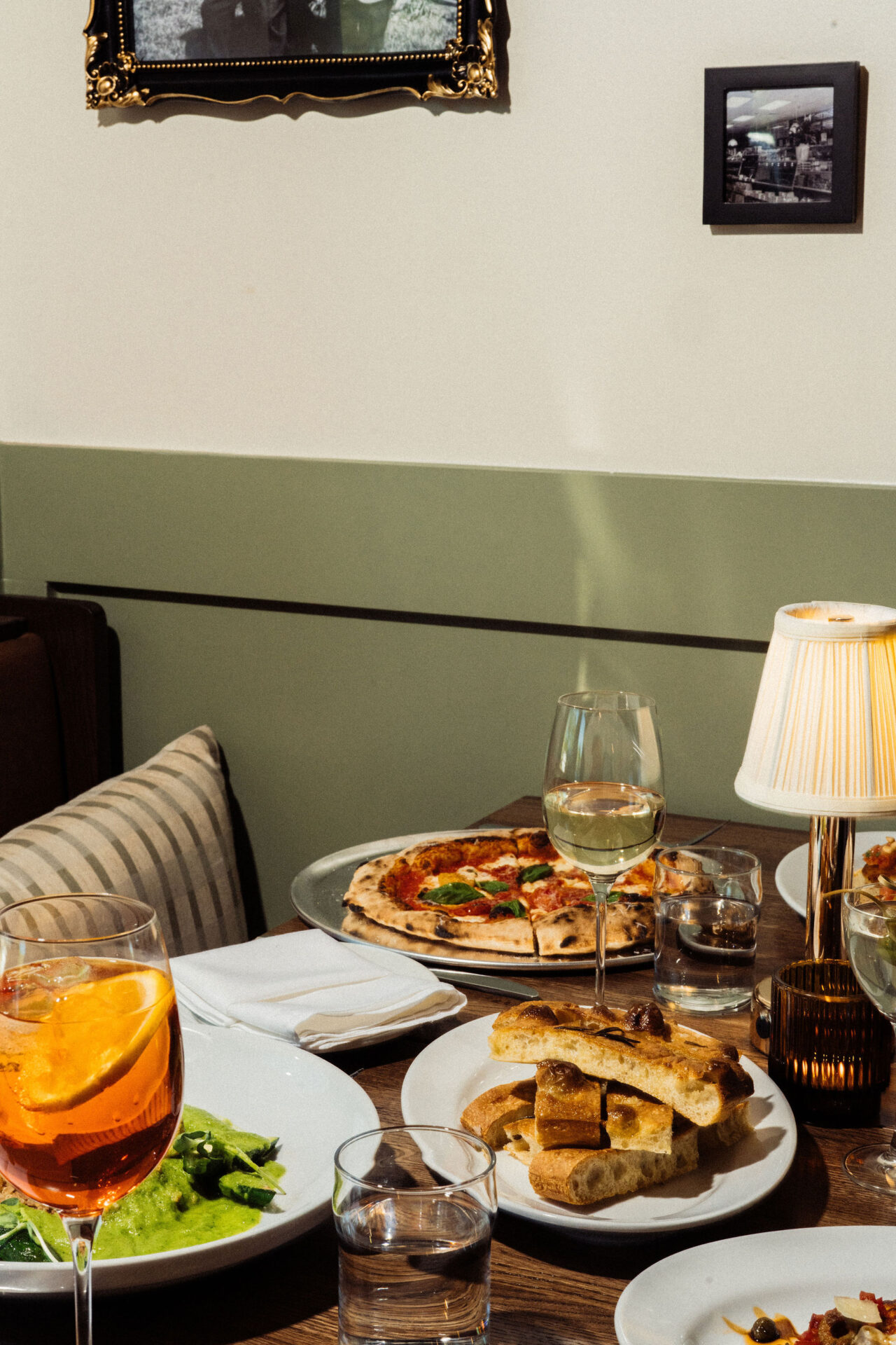 A table spread with pizzas, salad, and aperol spritzes joelle 