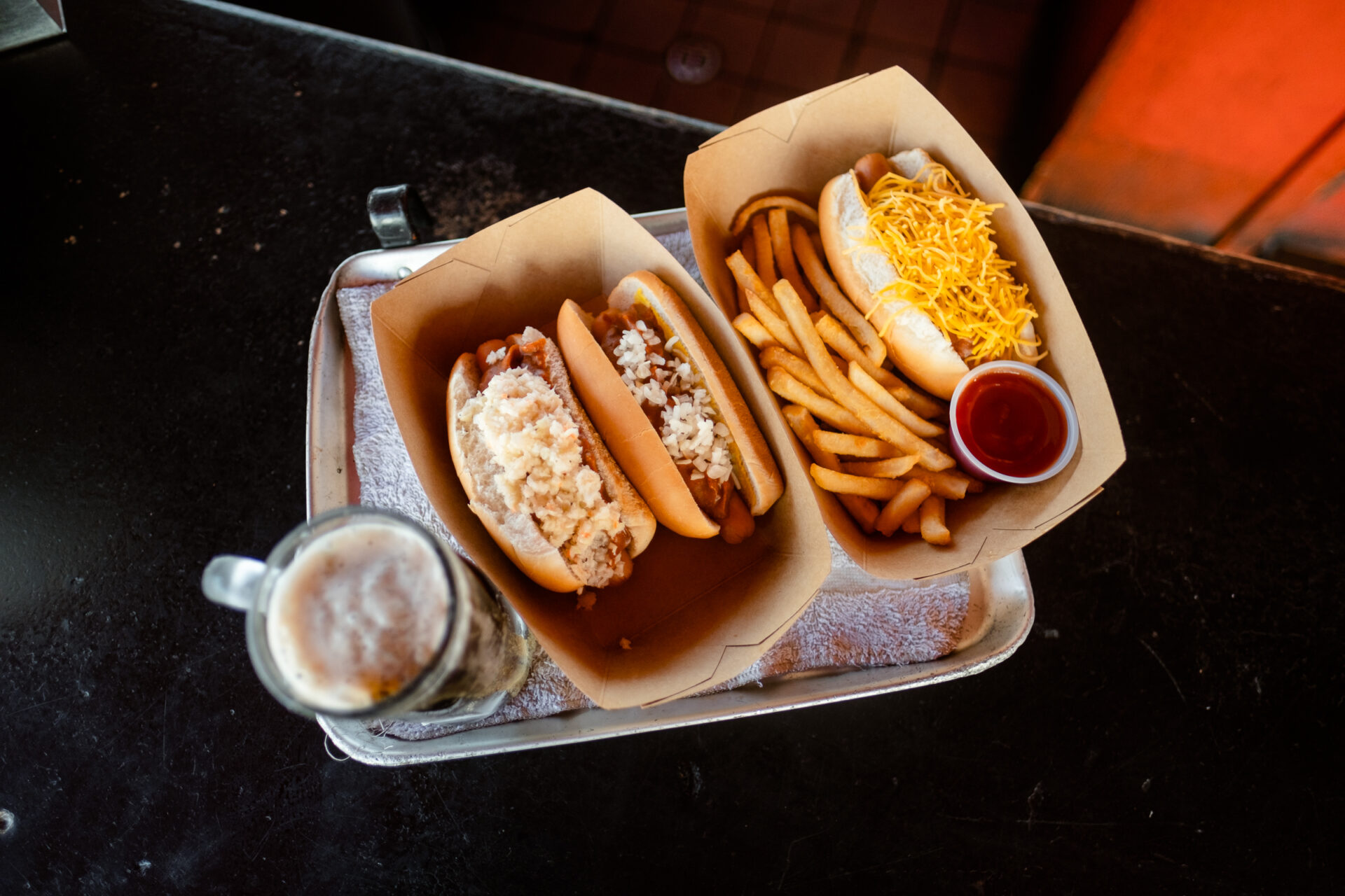 A root beer and three loaded hotdogs with a side of french fries on a tray at Stewarts Original Hot Dogs in Huntington, West Virginia.