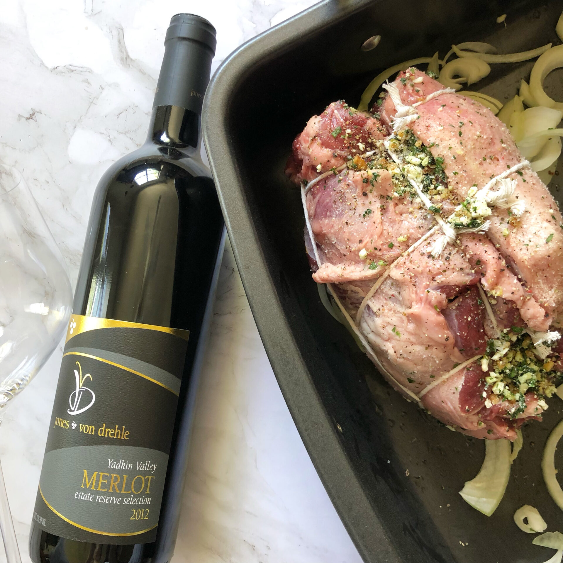 A raw stuffed roast beef in a serving pan about to be cooked and served with a bottle of Yellow Valley Merlot. 