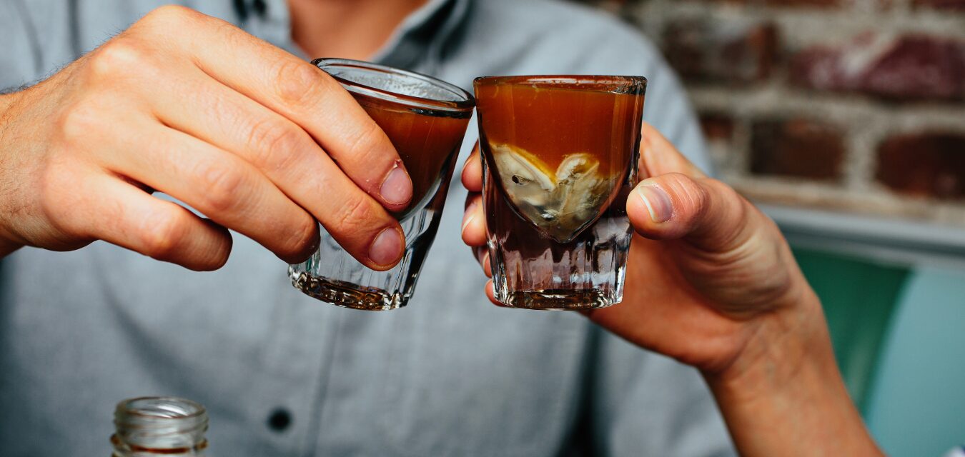 Two people toasting shot glasses full of dark liquid at The Darling Oyster Bar in Charleston, SC.