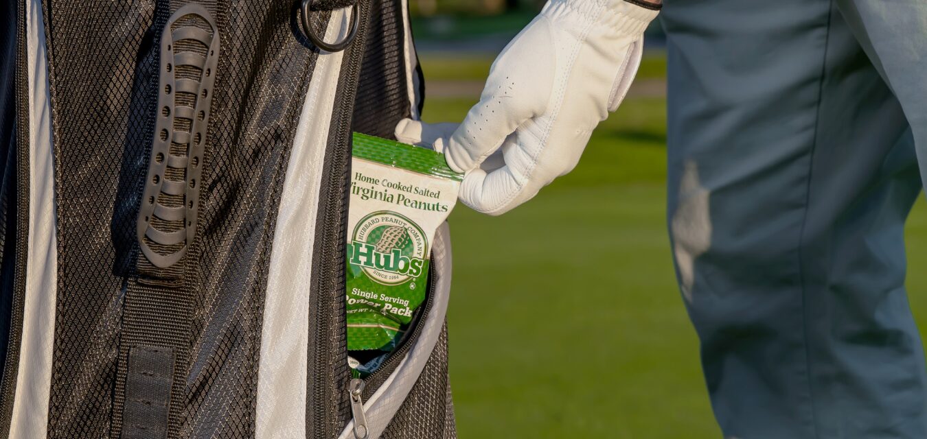 A golfer on the course pulling out a pack of Hubs Peanuts Power Packs as a snack.