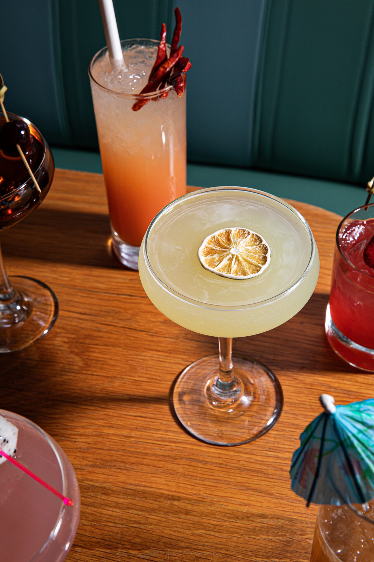 Several captivating, vibrant cocktails rest on a table at The Darling in Charleston, South Carolina. The focus is placed on a mild yellow cocktail with a dried lemon garnish. 