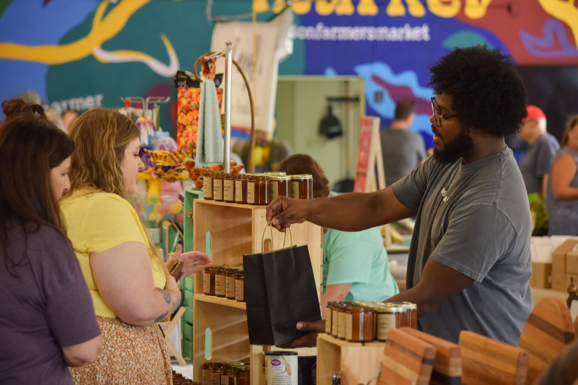 A vendor at Ruston Farmers Market in Ruston, Louisiana gives a black gift bag to two customers.