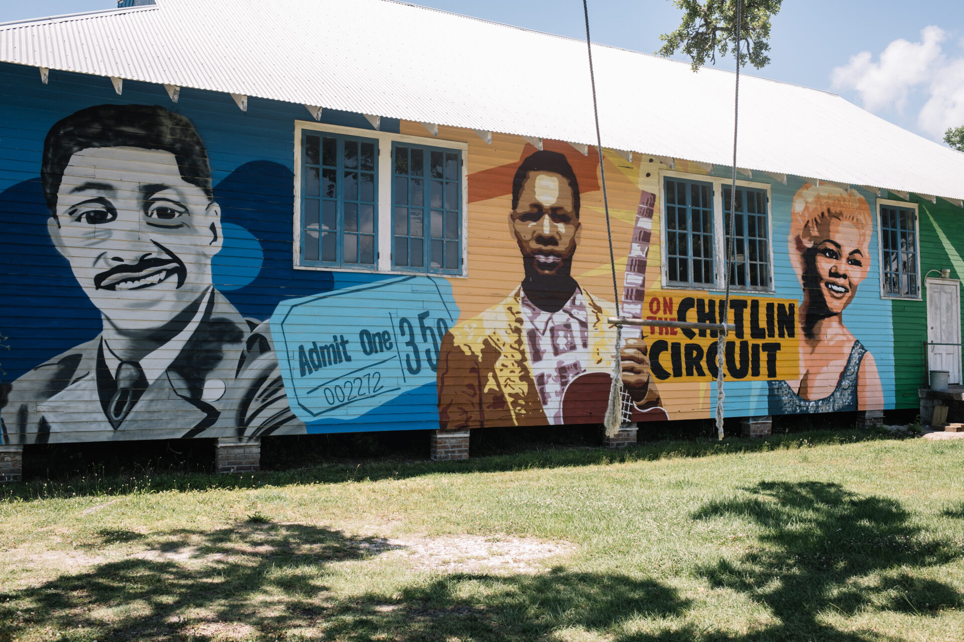 A colorful mural outside of 100 Men Hall in Bay St. Louis, Mississippi showcases various blues artists in blocks of blue, orange, and green.