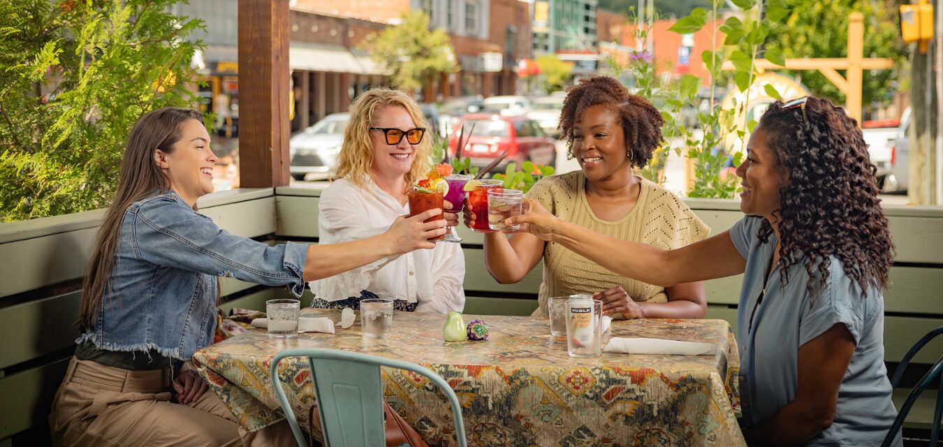 Three women sitting on a patio in Boone, North Carolina, cheering cocktails.