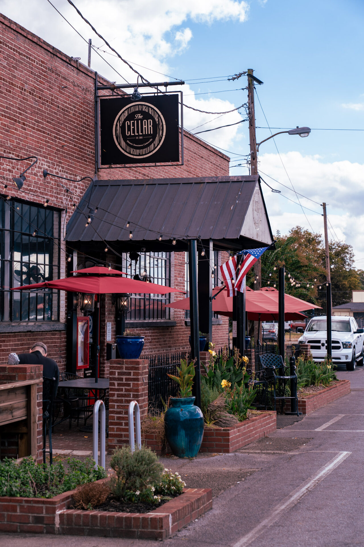 The Cellar, a red brick building with black metal finishes, shares the welcoming atmosphere of Cartersville, Georgia, also known as Museum City, through its outdoor seating and relaxed vibe.