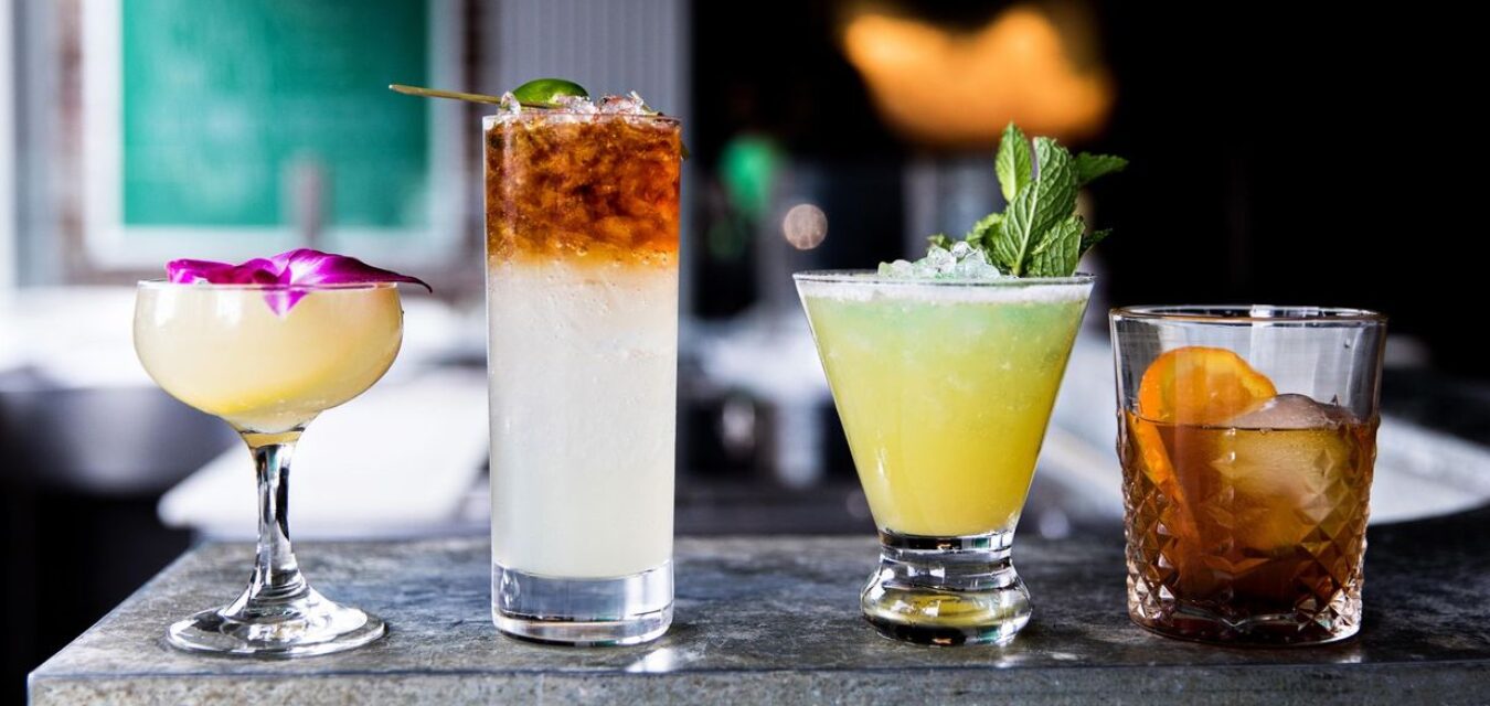 Four crisp cocktails line a modern, clean countertop at the Darling Oyster Bar in Charleston, South Carolina.