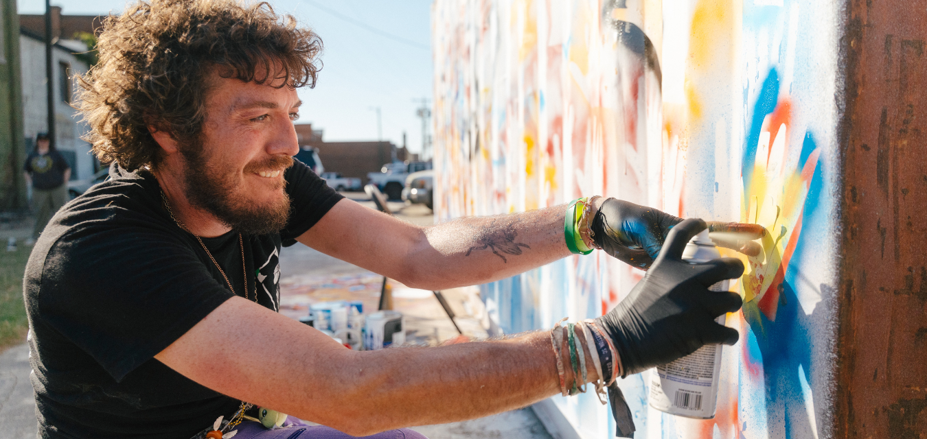 Caleb Braxton works on a mural on a shipping container that uses visitors hands in the underpaint process jpg